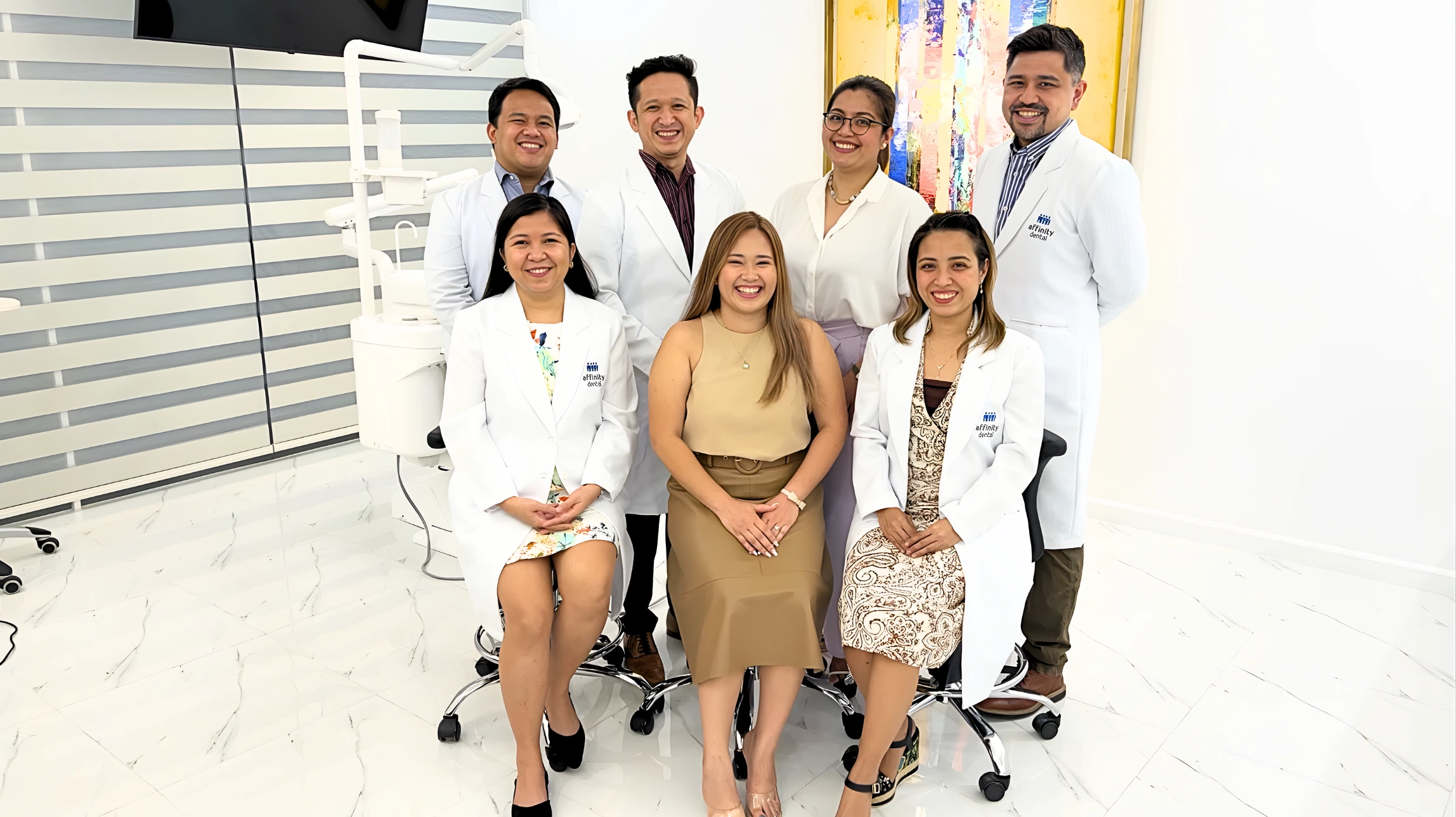 Group photo of the dentists of Affinity Dental Clinics Cebu, smiling inside one of the clinic’s modern treatment suites with bright interiors and dental equipment in the background.
