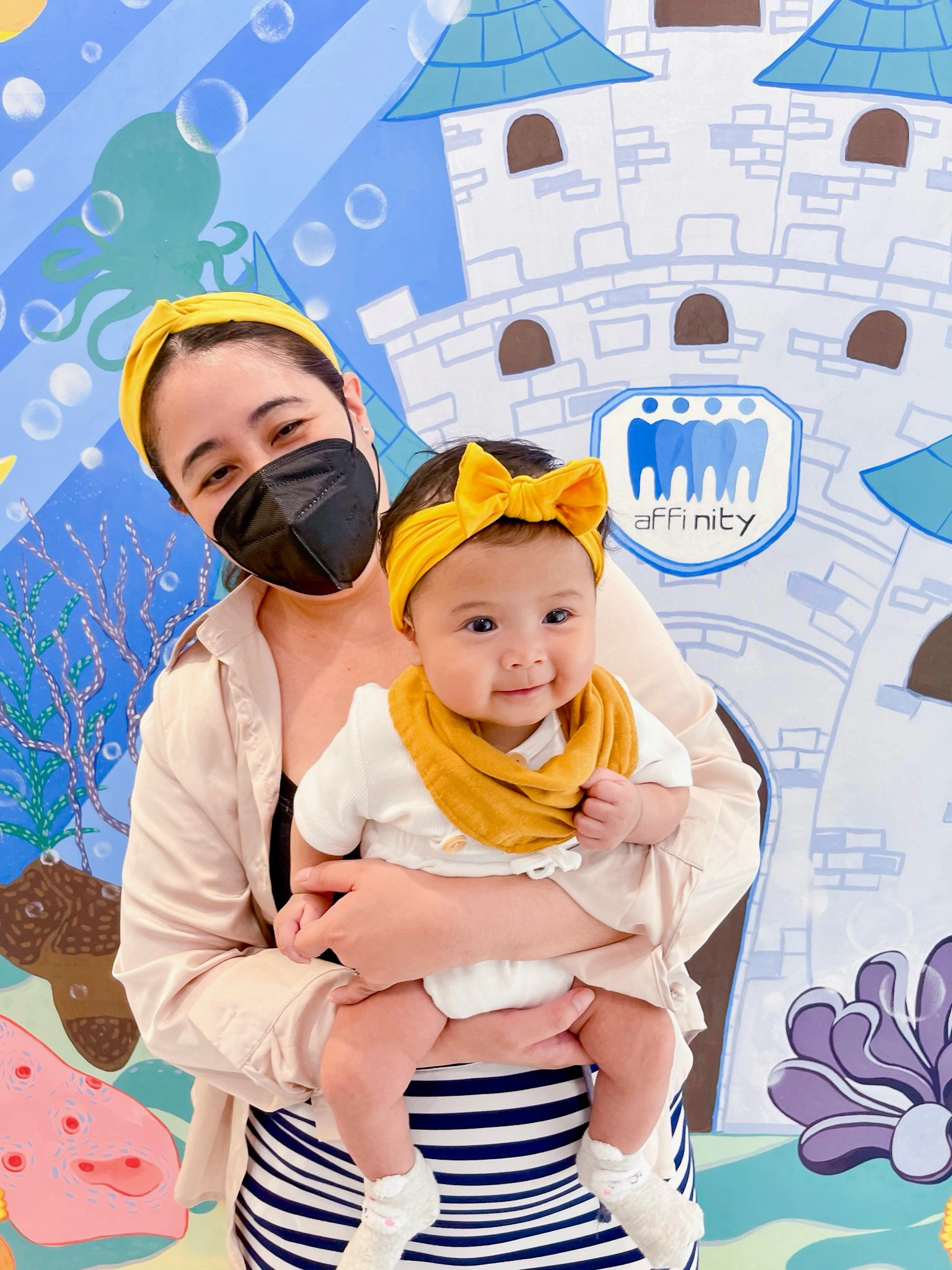 Mother holding her baby after an Age One Dental Visit at Affinity Dental Clinics Makati with colorful pediatric-themed background