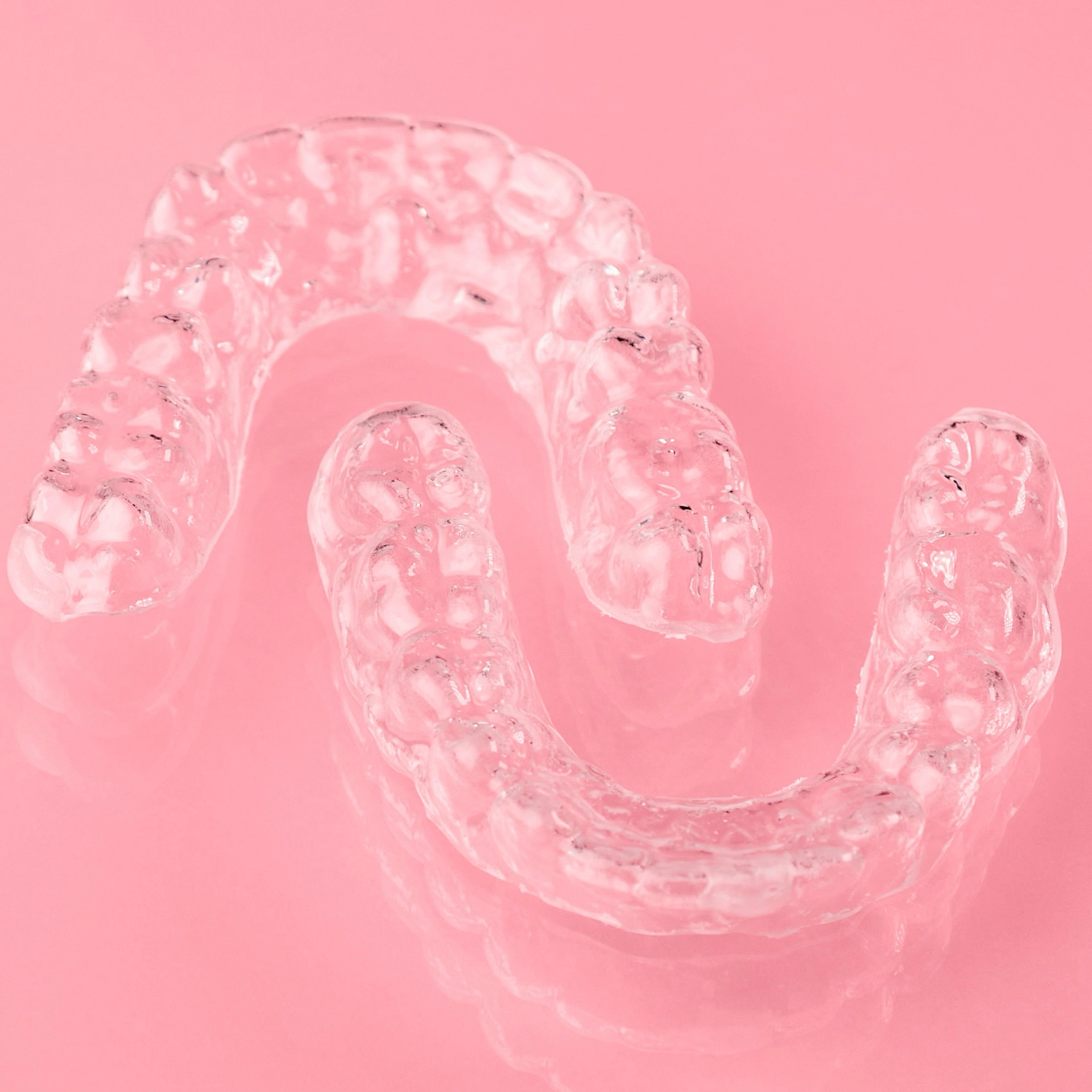 Set of upper and lower clear dental retainers displayed on a pink background