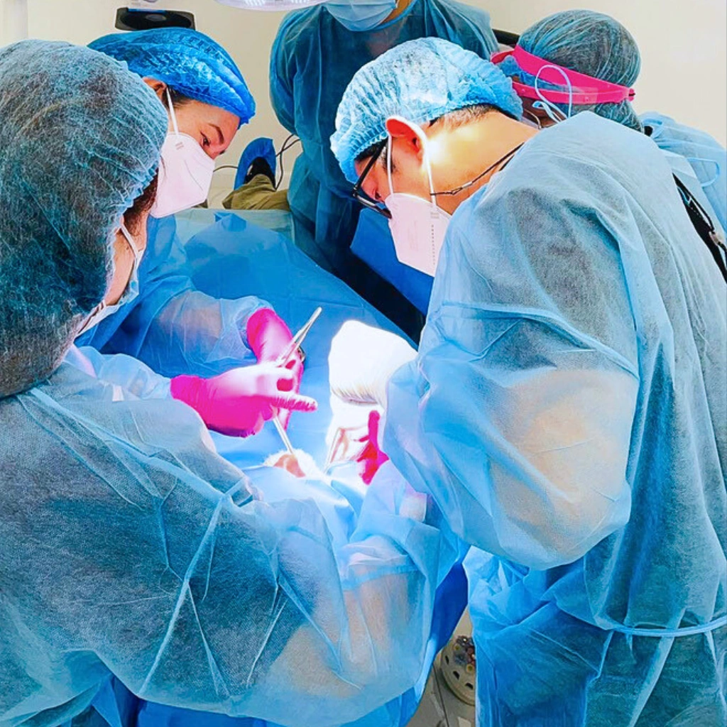 A team of dentists at Affinity Dental Clinics in blue surgical gowns, masks, and caps performing a sinus lift surgery under bright operating lights.