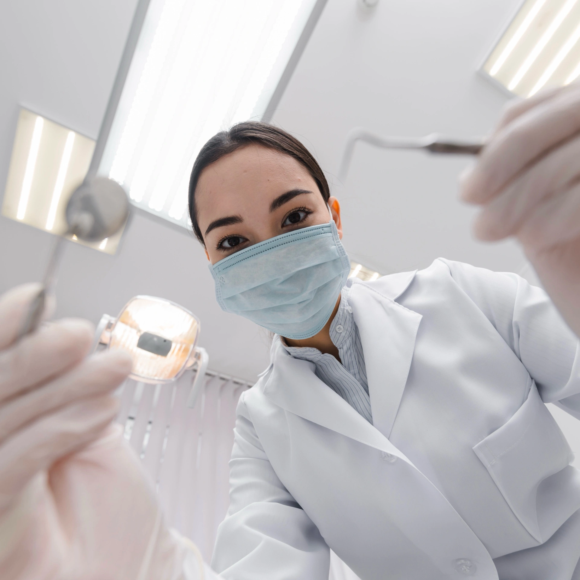 Female dentist in mask and gloves holding dental instruments, preparing for a general dentistry check-up.