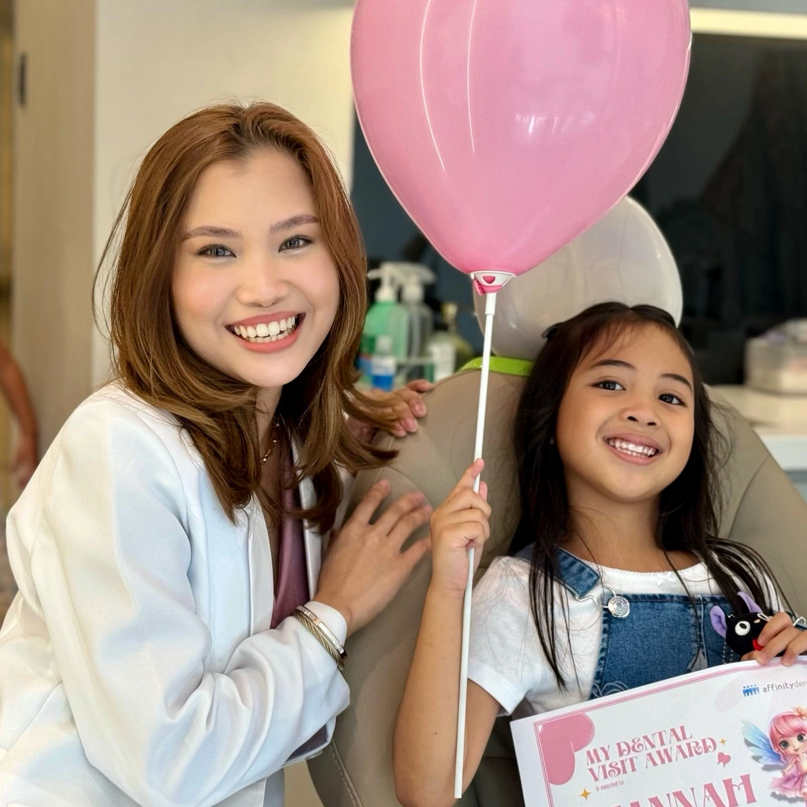 Dentist smiling with a young patient holding a balloon and certificate after a pediatric dental consultation at Affinity Dental Clinics BGC High Street