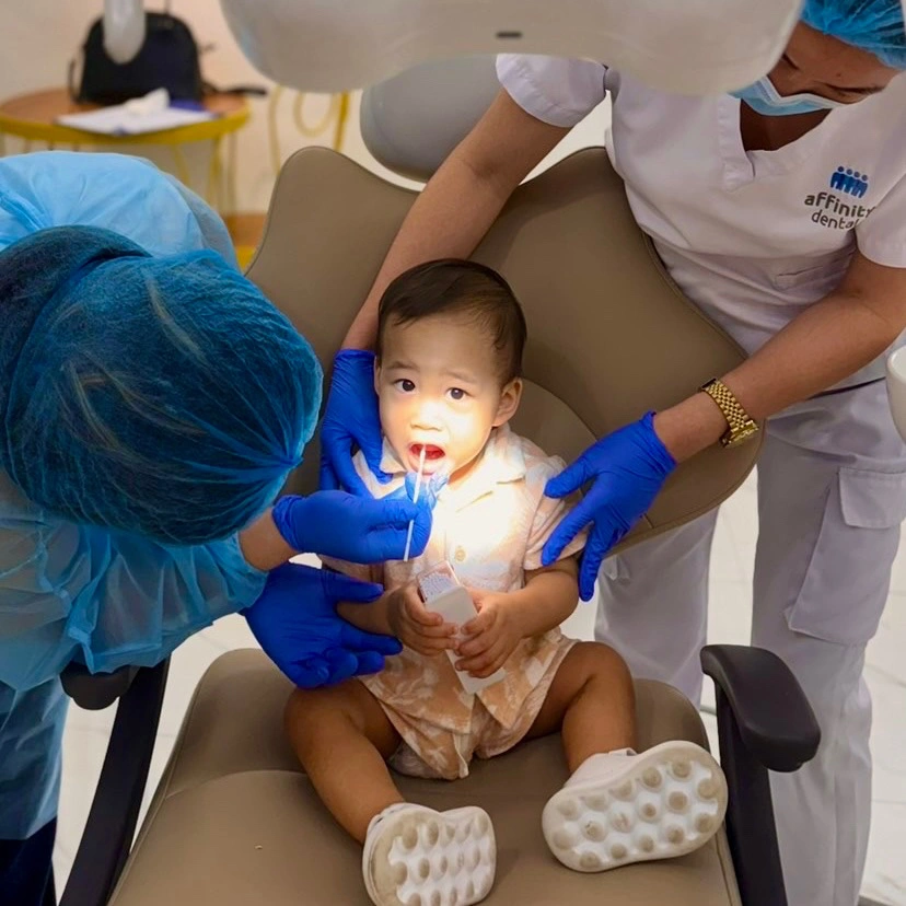 Toddler receiving fluoride treatment during a pediatric dental visit at Affinity Dental Clinics Cebu, guided by dentists and staff in protective gear