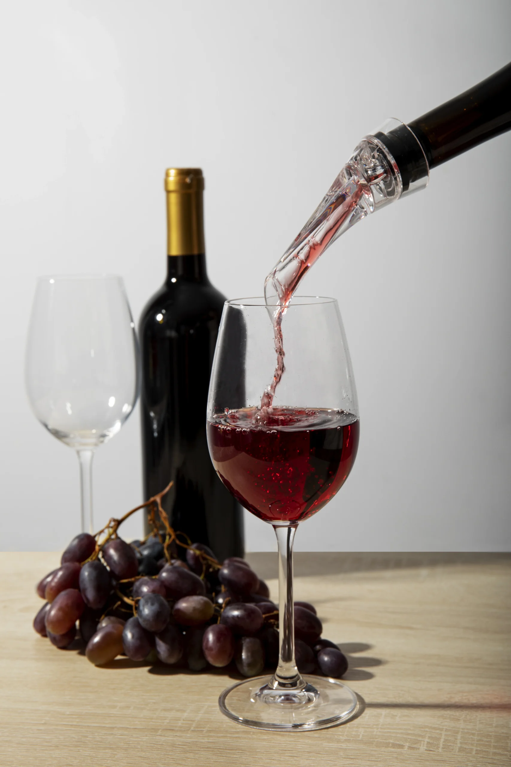 A glass of red wine being poured beside a wine bottle and grapes, illustrating one of the drinks to avoid after teeth whitening.