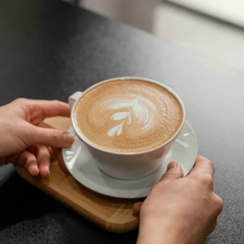 Hands holding a cup of coffee with latte art on a white saucer
